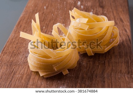 photo of raw tagliatelle with flour on brown wooden table