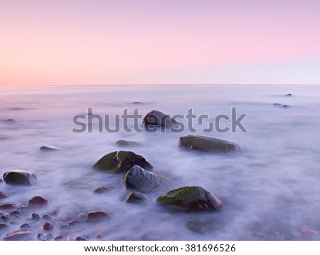 Pink sunset at rocky coast of sea. Slow shutter speed for smooth water level and dreamy effect