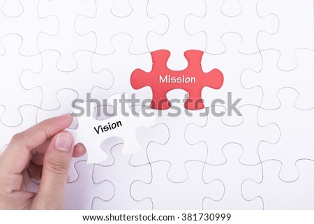 Hand embed missing a piece of puzzle into place, red space with word VISION MISSION. Business and financial concept.