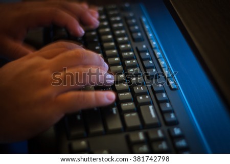 Hands typing keyboard in dim light. Taken with slow shutter to show the movement of the hands. Selective focus at the keyboard with shallow depth of field.