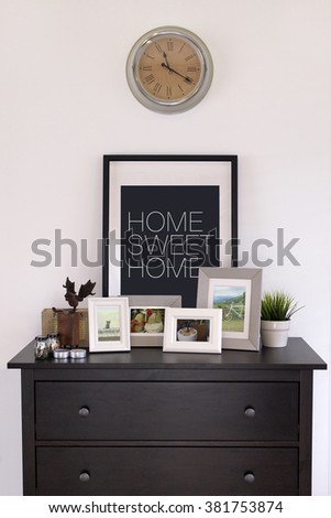 Picture frames collages on wooden cabinet with vintage clock in cozy living room, white concrete wall