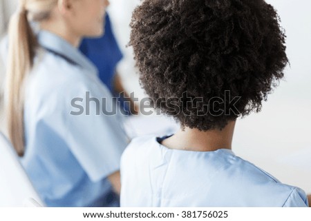 profession, people and medicine concept - close up of african female doctor or nurse with group of medics at conference in hospital from back