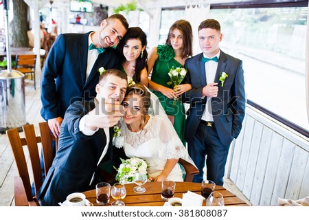 Happy friends of wedding couple and groomsman with bridesmaids at cafe make a selfie
