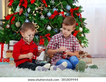 Two cute small brothers blows soap bubbles on Christmas tree background
