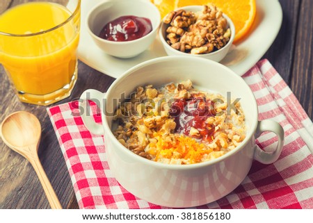 Oatmeal with walnuts, orange peel and jam for breakfast on rustic wooden background
