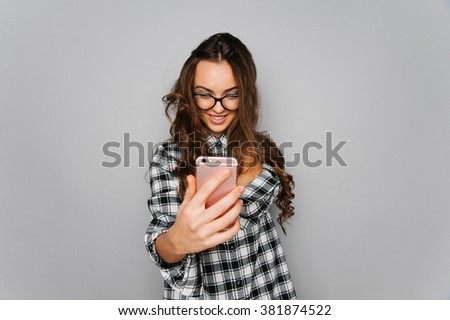 Portrait of cute teen girl texting emotional and making pictures to herself isolated on gray and studio background posing to the camera