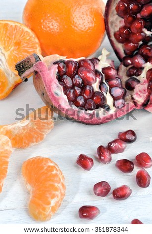 The photo shows the segments of an orange and ripe pomegranate on a white table close up