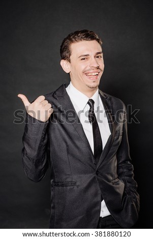 Portrait young angry businessman in black suit looking at camera and pointing finger at you camera gesture . happiness, gesture, emotions and people concept. Image on a black background.