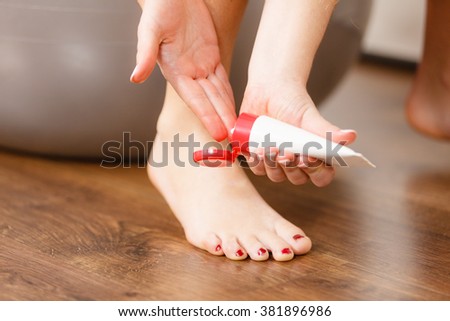 Woman fitness girl sitting on fit ball putting ointment cream on bad injured ankle. Sport training gym and injury foot problems 