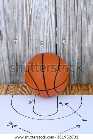 An orange basketball on a wood floor in front of a wood wall with set plans is a great image for basketball season, March Madness,or championship playoffs. Set plans are black on white. Copy space.