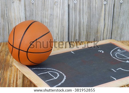 An orange basketball on a wood floor in front of a wood wall with set plans is a great image for basketball season, March Madness,or championship playoffs. Set plans are  on blackboard. Copyspace.