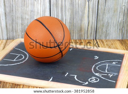 An orange basketball on a wood floor in front of a wood wall with set plans is a great image for basketball season, March Madness,or championship playoffs. Set plans are on blackboard. Copyspace.