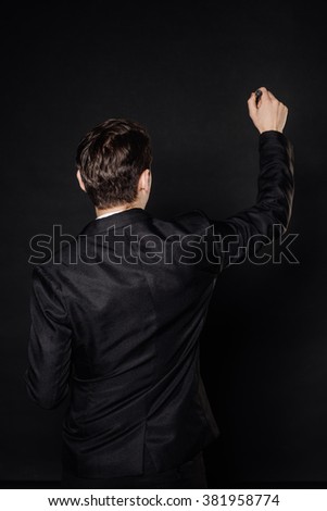 young businessman in black suit writing marker on transparent glass. emotions, facial expressions, feelings, body language, signs. image on a black studio background.