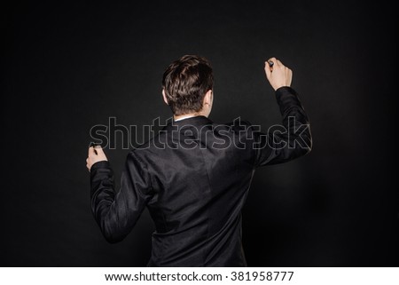 young businessman in black suit writing marker on transparent glass. emotions, facial expressions, feelings, body language, signs. image on a black studio background.