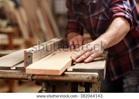 Cropped image of the hands of a skilled craftsman cutting a wooden plank with a circular saw in a workshop Royalty-Free Stock Photo #382064143