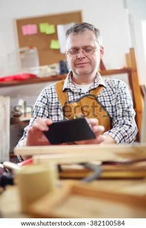 Portrait of carpenter sitting at his workshop use a digital tablet to take pictures.