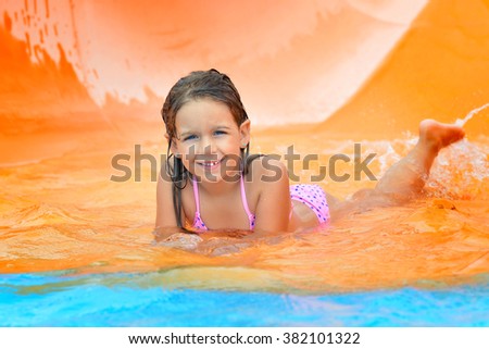 Real toddler girl enjoying her summer vacation on water slide at aquapark