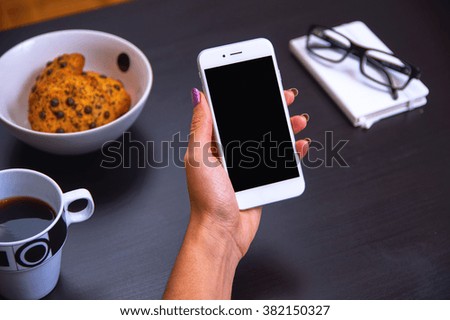 Modern smartphone with blank screen being held in woman's hand over black coffee table