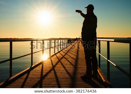 Man on pier photograph morning sea. Tourist with smart phone in hand. Fantastic morning with  smooth water level