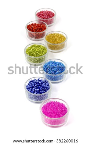 Row of glass bowls full of multicolored beads on white background