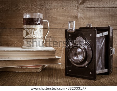 Old camera with tea in metal coaster and books on wooden background