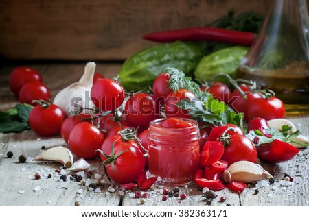 Tomato ketchup hot sauce with chili pepper and cherry tomatoes in a small glass jar, selective focus