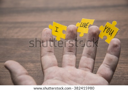 man's hand hold yellow jigsaw puzzle with a written word I Love You lie on brown table background  