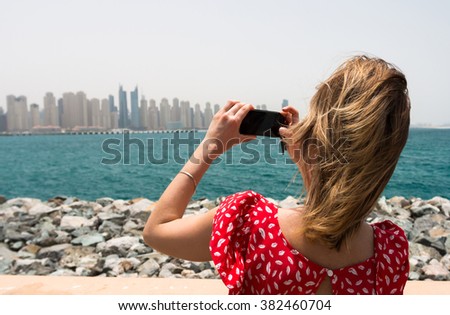 Rear view woman using a mobile phone to take a picture of the Dubai City