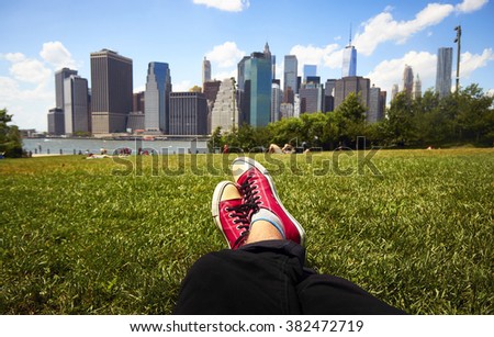 Feet in red sneakers in green grass in front of Manhattan, New York Royalty-Free Stock Photo #382472719