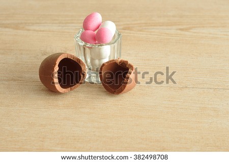 A broken chocolate easter egg filled with green and pink candy displayed on wooden background