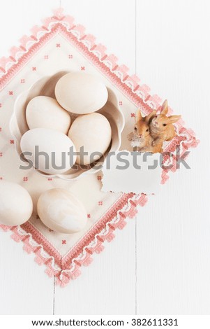 Vase with eggs, napkin and small rabbits on a white background