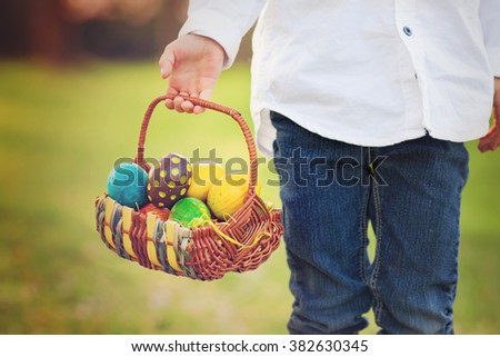 Cute adorable boy, gathering colorful easter eggs in a spring blooming cherry tree garden, smiling at the camera