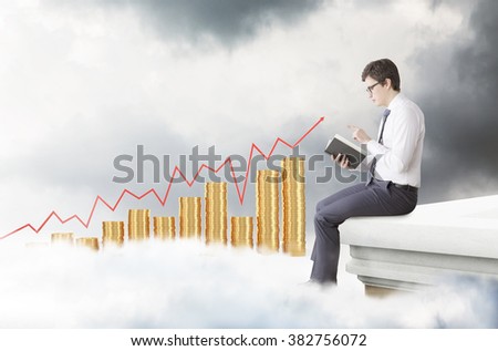 young man sitting on the edge of the roof and reading a book. Side view. Dark clouds, bar charts of coins and red graph at the background. Concept of studying