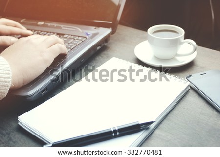 woman hand on computer with a phone, cup of coffee and notepad