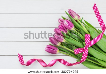 Bouquet of bright pink tulips decorated with pink ribbon on white wooden background. Top view, copy space