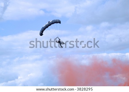 Parachutist coming into land through red smoke.