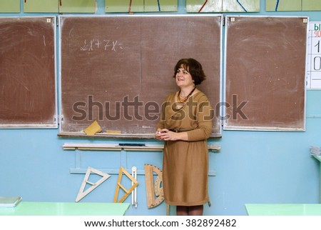Mathematics teacher stands at the blackboard in the classroom and holding chalk in hand