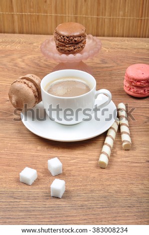 Cup of coffee with milk with french tasty macaroones on the wooden table in cafeteria. Sweet breakfast.
