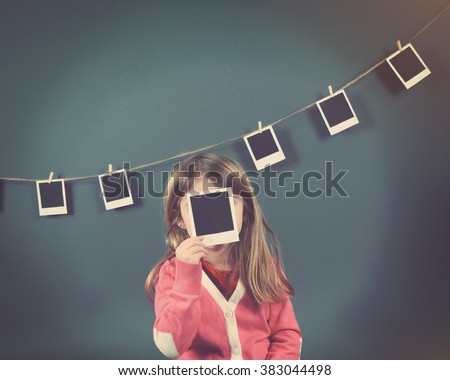 A little child photographer is holding up a photo of a blank film print and other photos on the wall for a art or creativity concept.