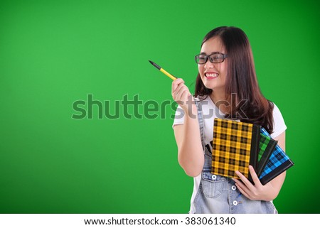 Funny nerdy school girl laughing cheerfully while pointing something at copy space with a pen, over green background