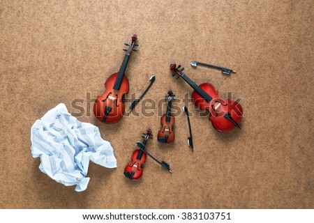 Four string musical orchestra instruments: violin, cello, contrabass, viola and crumpled sheet music lying near them on a wooden background. 