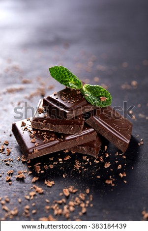 stack of dark chocolate and chocolate's crumbs. mint leaf on top of stack Royalty-Free Stock Photo #383184439
