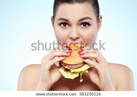 Funny girl eating hamburger on grey background