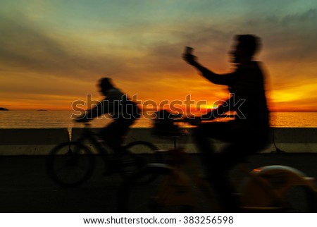 Silhouette of cyclist taking selfie near the sea during the sunset with motion blur also hdr effect applied