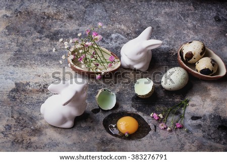 Quails Eggs  and white ceramic bunny with flowers and chocolate egg in an old spotted bowl against a rustic background with selective focus. A different type of concept image for Easter.