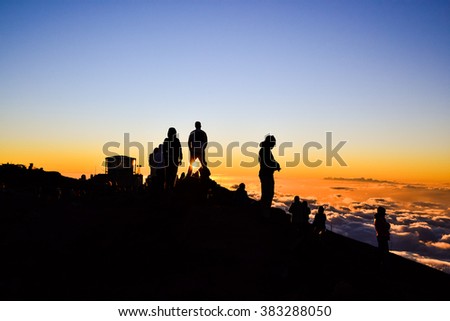 Tourists watching the spectacular sunset on the summit of Haleakala Crater (10,023 ft) on the island of Maui, Hawaii. Sun shining through the legs of a spectator. Observatories in the background.