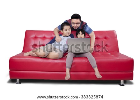 Picture of two cute children using laptop together with their father on the sofa while browsing internet online