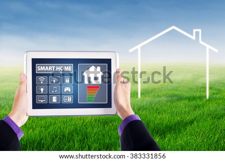 Image of hands holding a digital tablet with applications of smart home controller on the screen, shot at field