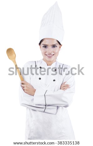 Picture of young female chef standing in the studio with confident pose and holding a spoon