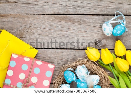 Easter background with blue and white eggs in nest, yellow tulips and gift box. Top view with copy space